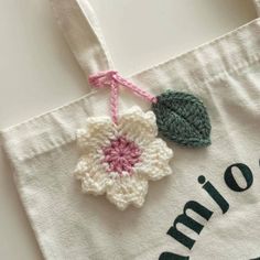 a crocheted flower is hanging from a tote bag with the name amino written on it