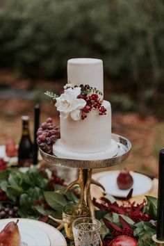 a white wedding cake sitting on top of a table covered in fruit and greenery