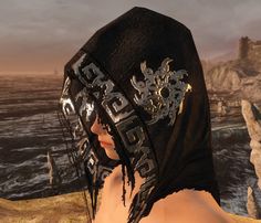 a woman wearing a black mask with gold and silver designs on her face near the ocean