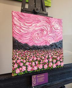 a painting is being displayed on a easel in front of a wall with flowers