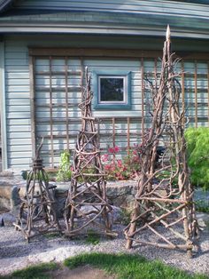 three wooden sculptures made out of sticks in front of a house with flowers on the side