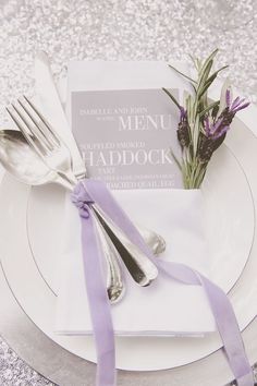 a table setting with silverware and purple ribbon