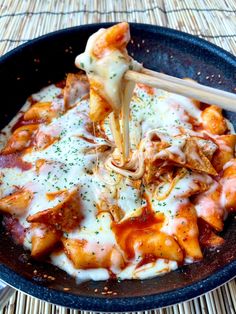 a skillet filled with pasta and cheese being held by chopsticks over it