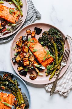 two plates with salmon, broccoli and other food on them next to silverware