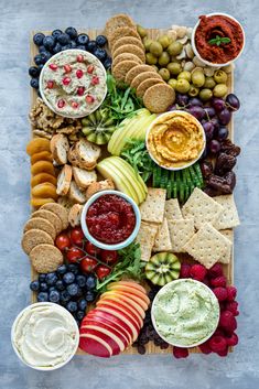 a platter filled with fruit, crackers and dips on top of a cutting board