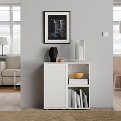 a white cabinet sitting in the middle of a living room next to a wall with pictures on it