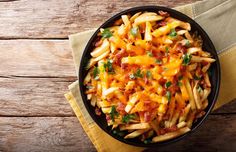 a bowl filled with pasta and cheese on top of a wooden table next to a napkin