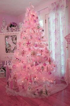 a white christmas tree with pink ornaments and lights in a room decorated for the holidays