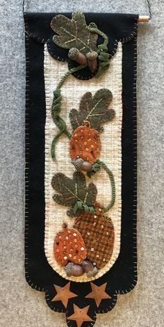 an embroidered wall hanging with pumpkins and leaves on it's side, along with stars