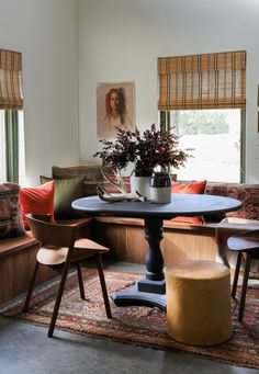 a living room filled with furniture and a round table in front of two windows covered in blinds