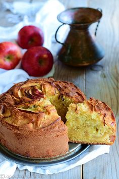 a cake on a plate with one slice cut out and apples in the back ground