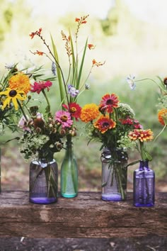 a group of vases filled with flowers sitting on top of a wooden table next to each other