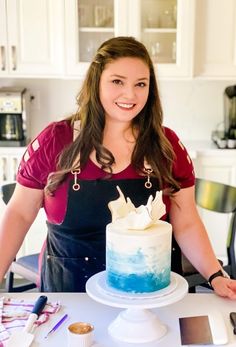 a woman standing in front of a cake with blue icing on it and smiling at the camera