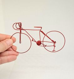 a wire sculpture of a bicycle being held by a person's hand on a white background