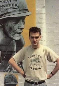 a man standing in front of a wall with posters on it and his hands on his hips