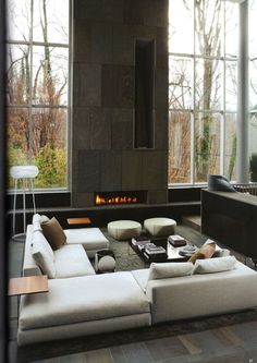 a living room filled with furniture and a fire place next to a large window that looks out onto the woods