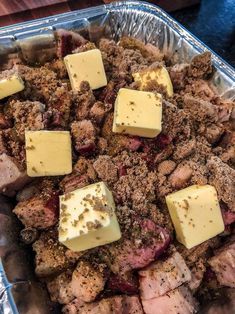 a pan filled with meat and cheese covered in seasoning next to a wooden table