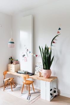 a wooden desk topped with a potted plant next to a mirror and two chairs