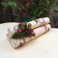 three logs are wrapped in twine and decorated with pine cones, berries and evergreens