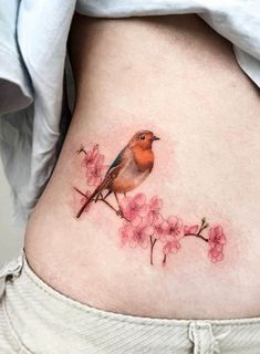 a small bird sitting on top of a tree branch with pink flowers in it's stomach