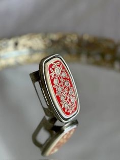 a red and white ring sitting on top of a silver table next to a mirror