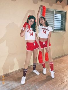 two women in cheerleader outfits holding red pom poms and posing for the camera