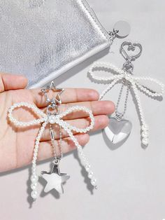 the hand is holding three charms with bows and hearts on them, one in white