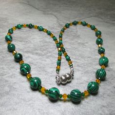 Two different sized and coloured Czech Crystal beads are combined with Green Malachite gemstone beads in this bright and colourful necklace. At each end of the necklace are five 4mm Malachite beads, then there are four 6mm Malachite's followed by three 8mm Malachite beads while finally in the centre are seven 10mm Malachite's. The Malachite beads are separated by an orange bicone Czech Crystal bead enclosed by two smaller green bicone Czech Crystal beads. All the metal work is Stainless Steel including the magnetic clasp and the earwires on the free matching earrings. Necklace and earring come enclosed within a gold foil fabric bag. Malachite ancient Greeks believe that Malachite reflects the heart of whoever hold it. Malachite is a protective stone that guards the bearer's heart from impu Green Malachite Round Beads, Polished Malachite Round Beaded Necklaces, Green Faceted Beads Spiritual Beaded Necklace, Malachite Gemstone Beaded Necklaces, Green Spiritual Beaded Necklace With Spacer Beads, Green Spiritual Beaded Necklace With Faceted Beads, Round Malachite Beaded Necklace, Spiritual Green Beaded Necklace With Spacer Beads, Beaded Malachite Round Bead Necklaces