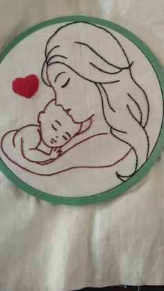 a hand embroidered picture of a woman holding a baby in her arms with a red heart on it