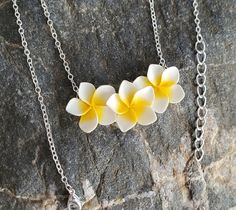 three white and yellow flowers are on a silver chain with a black stone behind them