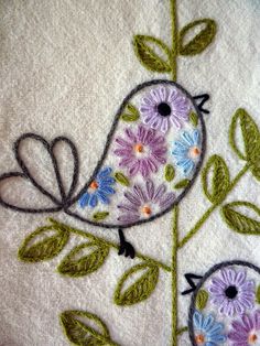 a close up of a bird on a branch with leaves and flowers embroidered onto it