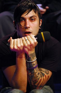 a tattooed man sitting in front of a microphone with his hands clasped to his face