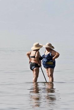 two people standing in the water with their backs to each other, wearing hats and holding paddles