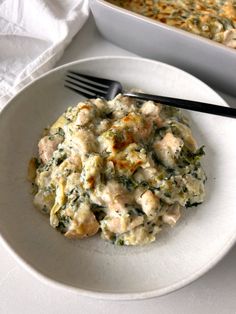 a white plate topped with chicken and spinach casserole next to a fork