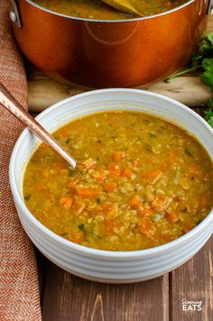 a bowl of soup with carrots and celery next to a pot of bread