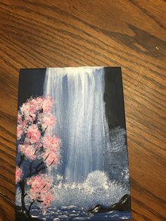 a painting on a wooden table with a tree and waterfall in the background that has pink flowers