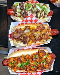 three loaded hot dogs sitting on top of paper plates