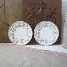 two white and gold plates sitting on top of a bed next to a wooden headboard