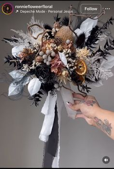 a person is holding a bouquet with flowers and feathers on it in front of a gray background