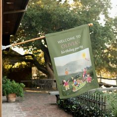 a welcome sign hanging from a clothes line in front of a brick walkway and trees