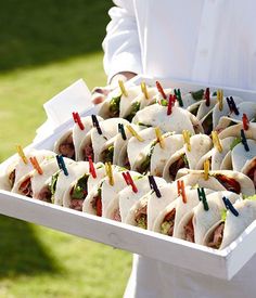 a man holding a tray full of tasty looking appetizers with toothpicks stuck in them