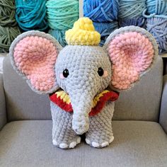 a crocheted elephant with a yellow hat on it's head sits in front of yarn balls