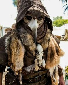 a man dressed up as a bird with a hood and feathers on his head, holding a dead animal in his hand