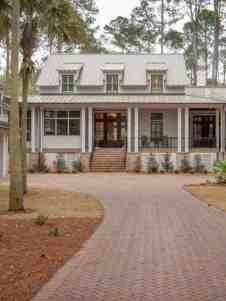 a large white house surrounded by trees and grass in the middle of a driveway with a brick walkway leading to it