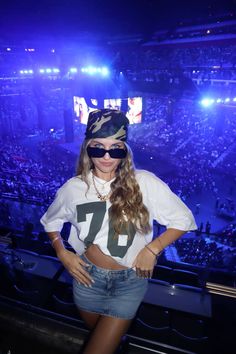 a woman wearing sunglasses and a camo hat stands in front of an audience at a concert