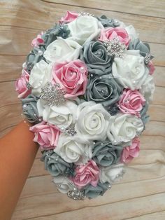 a bridal bouquet with pink and grey flowers on it, held by someone's hand