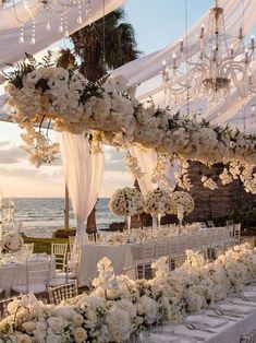 an outdoor wedding setup with white flowers and chandeliers at the head table, overlooking the ocean