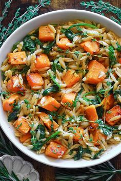 a white bowl filled with pasta and carrots on top of a table next to silverware