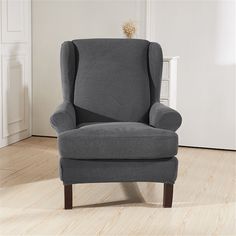 a gray chair sitting in a living room next to a white wall and wooden floor