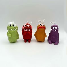 three different colored toy monsters sitting next to each other on a white surface with eyes